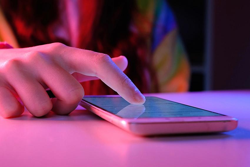 Use of mobile phone in trendy neon lights. Creative vivid color of ultraviolet red and blue. Hands of Teen Girl scrolling up photos Close-up at dark n...